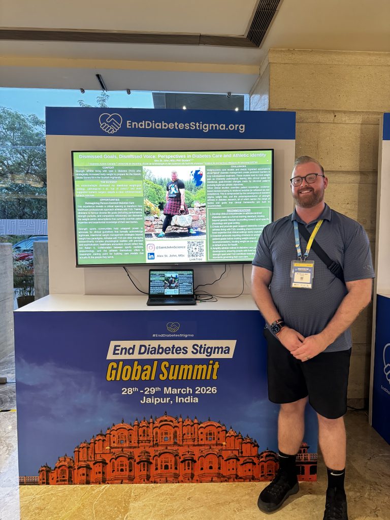 Alex wearing a conference badge stands smiling beside a digital research poster display at the End Diabetes Stigma Global Summit. The poster, titled “Dismissed Goals, Dismissed Voice: Perspectives in Diabetes Care and Athletic Identity,” is shown on a large screen above a laptop. Summit branding and signage are visible on the display booth.