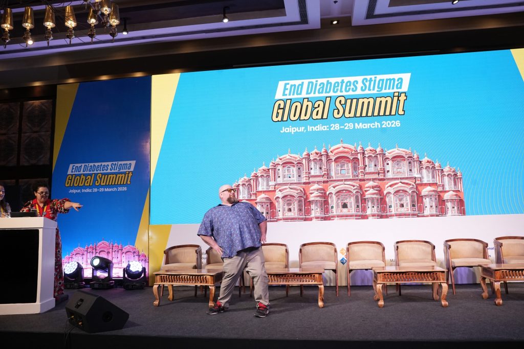 Al Martin on a large stage with a blue backdrop that reads 'End Diabetes Stigma Summit." Al is posing like a model on stage.